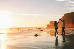 Paar tanzt fröhlich am Strand bei Sonnenuntergang – ein emotionaler Moment voller Liebe festgehalten bei einem Fotoshooting auf Mallorca