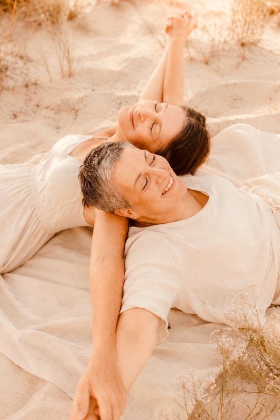 Zwei Frauen mit tiefer Freundschaft liegen lachend im Gras – ein authentischer Moment eingefangen in emotionaler Fotografie.
