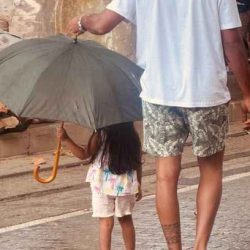 Familienmoment im Regen – Kind und Erwachsener unter einem Schirm, begleitet von Essence of Love bei emotionalen Lebensgeschichten